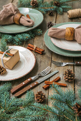 Beautiful table setting with Christmas branches, fir cones and cinnamon on wooden background, closeup