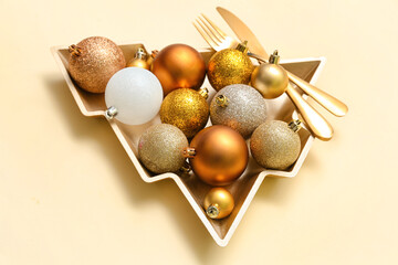 Beautiful plate in shape of Christmas tree with balls and cutlery on beige background