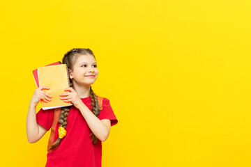 A little girl holds school notebooks in her hands. the child is preparing for school on a yellow isolated background. Copy Space.