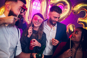 Multiracial friends celebrating new years eve with party props and drinks in the club
