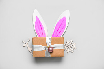 Paper bunny ears with gift and Christmas decor on grey background