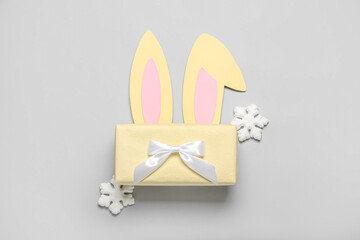 Paper bunny ears with Christmas gift and snowflakes on grey background