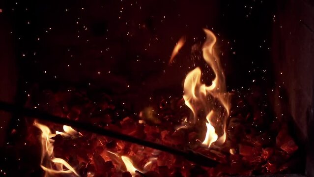 A fireplace poker stirs the coals in a fireplace causing sparks to rise. Slow Motion.