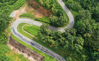 Aerial view drone fly over countryside road passing through the green forest and mountain in Thailand. Mountain winding zig zag road. Top aerial view
