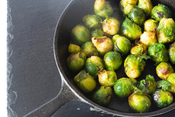 Sprouts fried, in a cast iron frying pan wiyth olive oil, on a slate board. Isolated on a white background