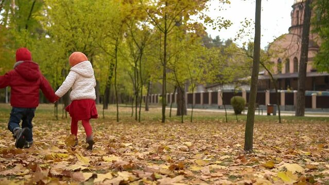 Two happy funny active smilling friends children kids boy Girl walking running holding hands in park forest enjoying autumn fall nature weather. Kid in red cloth playing hiding behind trees Slow