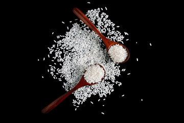 White uncooked rice in wooden spoons on black background. Raw grains of long rice.