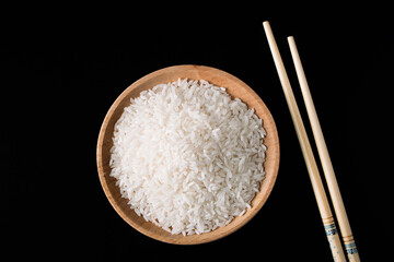 Fototapeta na wymiar Raw white rice and chopsticks on black background. Long uncooked rice in wooden plate.