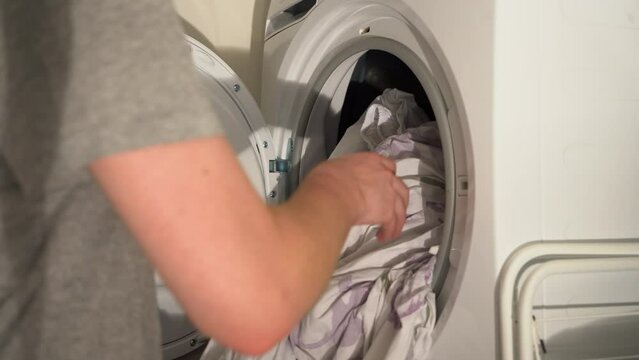 Young Caucasian adult pulls warm laundry bed sheets from clothes dryer
