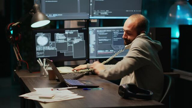 Software developer talking on landline phone at night, answering phone call in office. Male programmer using telephone with cord to chat and work on online cloud computing, artificial intelligence.