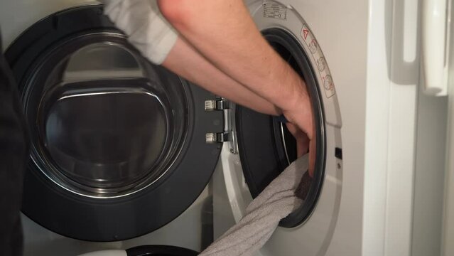 Close up: Young man empties washing machine into laundry basket