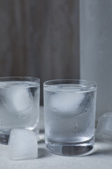 Shot glasses of vodka with ice cubes on light grey table