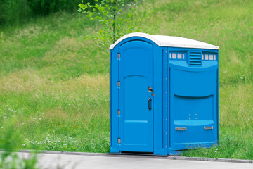 Blue portable toilet near road in green park