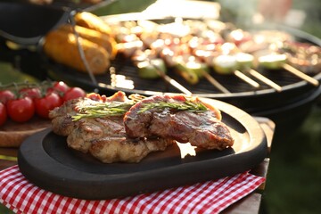 Tasty cooked meat and cherry tomatoes on table near barbecue grill outdoors