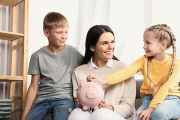 Happy family putting coin into piggy bank at home