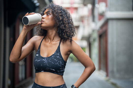 African Woman Sport Healthy Fit And Firm Slim Drink Water From Cup On The Hand. Athletic Running Wearing In The Sportswear At City And Town. Fitness And Sport Motivation. Runner Concept.