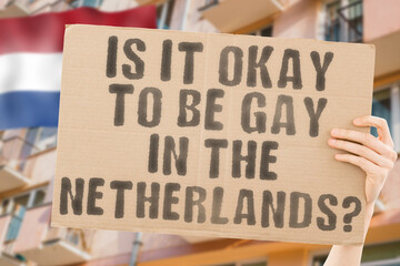 The question " Is it okay to be gay in the Netherlands? " is on a banner in men's hands with blurred background. Friendly. Passionate. Contact. Date. Dating. Lover. Partner. Boyfriend. Pleasant