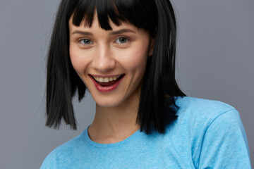 a beautiful, sweet, relaxed woman stands on a light background in a blue T-shirt and looks at the camera with a pleasant smile. Horizontal photo with empty space