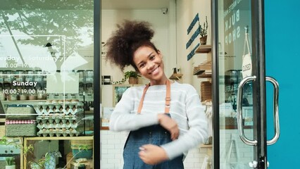 Young African American female shopkeeper opening glass door, happy smile, works at refill store, zero waste, plastic-free grocery shop, eco-friendly SME. Thai language on a label at door means "pull"