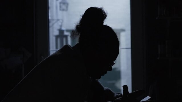 Woman silhouette in the dark kitchen while being on her phone.
