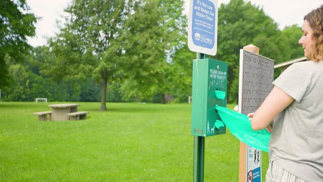 Dog owner cleaning up after dog with waste bag from bin at park