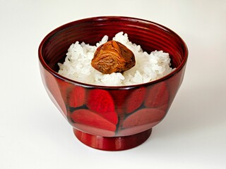 Tokyo,Japan - November 18, 2022: Closeup of hot rice with Umeboshi or pickled plum in a lacqure ware bowl on white background
