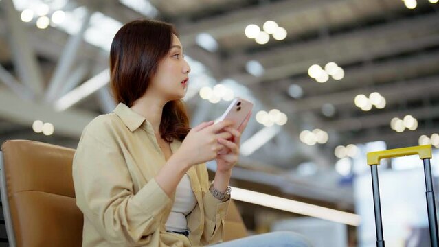 Asian woman waiting for departure at the airport on vacation holiday. Asia female passenger using mobile smart phone and sitting in terminal hall while waiting for her flight