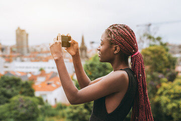 A side profile shot of a young black woman tourist taking a panoramic picture of the cityscape via...