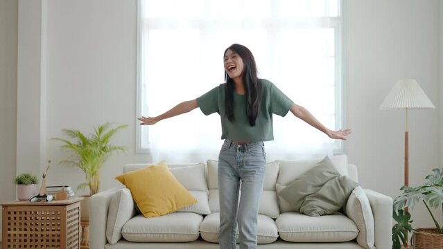 Young asian woman dancing on the floor in living room at home. Happy asia female smile relaxing in house, healthy mental wellness and wellbeing