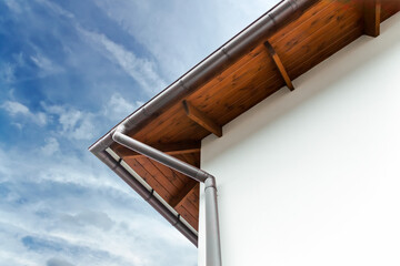gutters and downspout on the corner of a house. wooden roof structure.