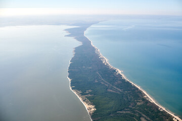 Aerial view from airplane window to Curonian spit in Kaliningrad Oblast, Russia, beautiful green forest and sandy beach on curved sand dune spit between Baltic sea. Aerial view to Kurshskaya kosa - obrazy, fototapety, plakaty