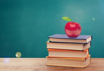 Set of books with fresh apple on desk