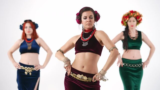 Three attractive women posing performing belly dance in slow motion at white background. Front view portrait of confident Caucasian belly dancers dancing looking at camera