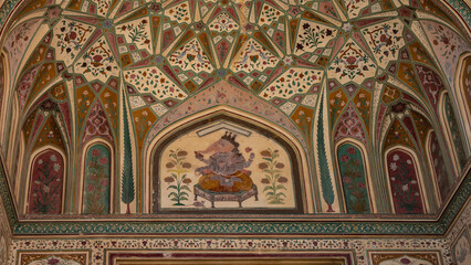A fragment of an ancient painting on the ceiling. The God Ganesha is depicted on a couch surrounded by geometric and floral designs. India. Jaipur Amber Fort