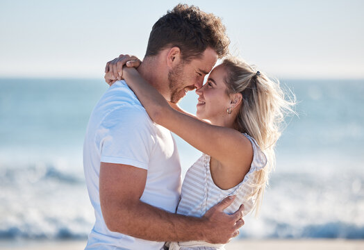 Couple, love and hug at the beach together, nose touch and bonding with travel and date by the ocean for summer holiday. Happy, man and woman with quality time, sea waves and romantic out in nature.