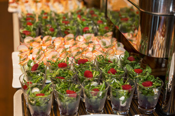 Portioned salads with arugula and raspberries in small glasses on the buffet table. Holidays,...