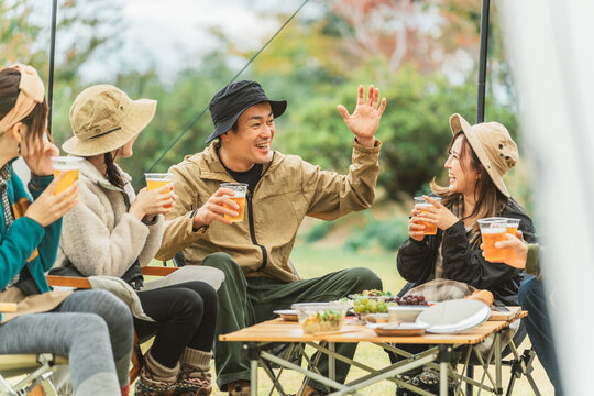 秋冬のキャンプ場で仲間と一緒にビールを飲みながら冗談を言って盛り上げる人気者のアジア人男性
