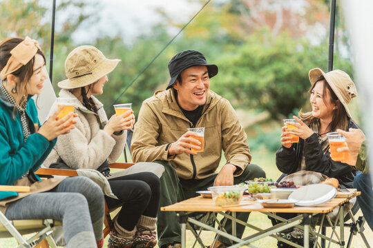 秋冬のキャンプ場で仲間と一緒にビールを飲んでパーティーするアジア人の男女
