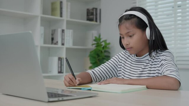 training  and learing online course for Asian children. video conference on laptop at home. play back online course, girl student wear earphones to study, notes homework, video classes, new education.