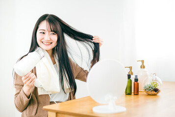 ドライヤーを使って髪を乾かす日本人女性（笑顔）
