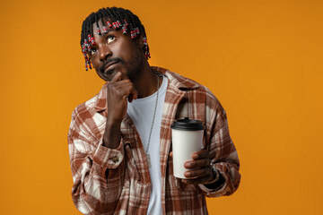 Young african man holding cup of take away coffee over yellow background