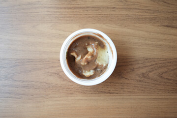 mashed potatoes with gravy sauce in a white cup plastic on wooden background.