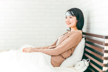ベッドで休む冷却シートをつけた笑顔のアジア人女性

