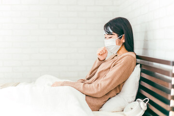 風邪をひいてベッドで咳をする体調不良の女性（冷却シート・マスク）

