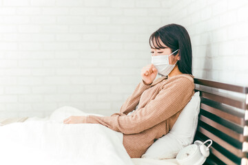 風邪をひいてベッドで咳をする体調不良のマスクをしたアジア人女性
 - obrazy, fototapety, plakaty