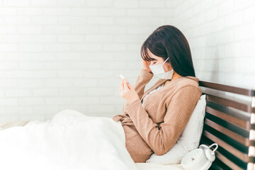 頭痛と発熱で苦しむ風邪をひいたマスク姿の日本人女性
