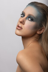 Make-up and fashion concept. Studio portrait of beautiful woman with fancy and futuristic blue, gray make-up and brown lipstick. Blonde model looking at camera with blue eyes and seductive look