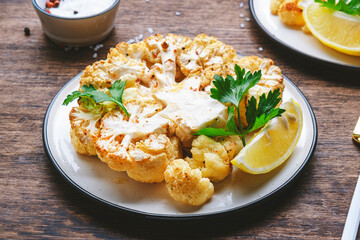 Baked cauliflower steak on plate, rustic wooden table background, top view