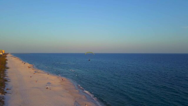 A lone paraglider flying peacefully over the ocean and beach at the end of the day,