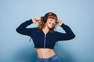 Happy young woman dancing while listening to music on headphones in a studio